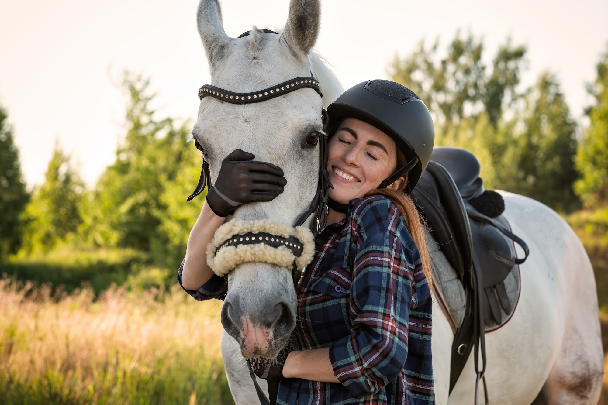 Young caucasian beautiful woman taking care of her horse walking at field.